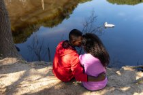Feliz pareja diversa sentada en el lago en el campo. estilo de vida al aire libre saludable y activo y tiempo libre. - foto de stock