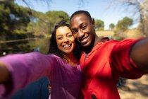 Feliz pareja diversa tomando selfie en el lago en el campo. estilo de vida al aire libre saludable y activo y tiempo libre. - foto de stock