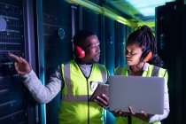 Afrikanische Computertechniker mit Kopfhörern und Laptop arbeiten im Serverraum. digitale Informationsspeicherung und Kommunikations-Netzwerktechnologie. — Stockfoto