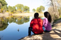 Happy diverse couple sitting by the lake in countryside. healthy, active outdoor lifestyle and leisure time. — Stock Photo