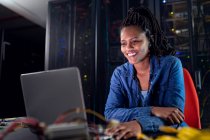 Técnico de computación afroamericana usando portátil que trabaja en la sala de servidores. tecnología de redes digitales de almacenamiento y comunicación de información. - foto de stock