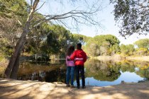 Feliz casal diversificado em pé no lago no campo. saudável, estilo de vida ao ar livre ativo e tempo de lazer. — Fotografia de Stock