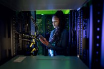 African american female computer technician using tablet and working in server room. digital information storage and communication network technology. — Stock Photo