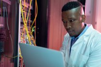 African american male computer technician using laptop working in business server room. digital information storage and communication network technology. — Stock Photo