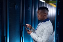 Tecnico informatico afroamericano di sesso maschile che indossa cuffie utilizzando tablet che lavorano nella sala server. tecnologia digitale di memorizzazione delle informazioni e rete di comunicazione. — Foto stock
