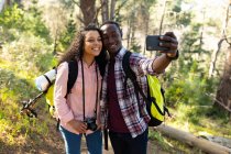 Feliz casal diversificado com mochilas tomando selfie e caminhadas no campo. saudável, estilo de vida ao ar livre ativo e tempo de lazer. — Fotografia de Stock