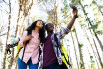 Happy diverse couple with backpacks taking selfie and hiking in countryside. healthy, active outdoor lifestyle and leisure time. — Stock Photo
