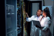 Técnicos de informática afro-americanos usando laptop trabalhando na sala de servidores. armazenamento digital de informações e tecnologia de rede de comunicação. — Fotografia de Stock