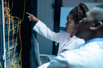 African american computer technicians using laptop working in server room. digital information storage and communication network technology. — Stock Photo