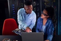Técnicos informáticos afroamericanos que usan computadoras portátiles que trabajan en la sala de servidores. tecnología de redes digitales de almacenamiento y comunicación de información. - foto de stock