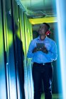 Técnico de computadoras afroamericano usando auriculares usando tableta trabajando en la sala de servidores. tecnología de redes digitales de almacenamiento y comunicación de información. - foto de stock