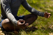 Relajante hombre afroamericano sentado con las piernas cruzadas y meditando en el campo. estilo de vida al aire libre saludable y activo y tiempo libre. - foto de stock