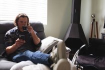 Кавказький інвалід п'є каву і користується смартфоном, який сидить вдома на дивані. інвалідність і гандикап — стокове фото