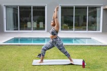 Focada afro-americana plus size mulher praticando ioga no tapete no jardim por piscina. fitness e estilo de vida saudável e ativo. — Fotografia de Stock