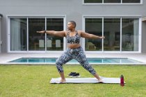 Africano americano enfocado más mujer del tamaño que practica yoga en la estera en el jardín por la piscina. fitness y estilo de vida saludable y activo. - foto de stock