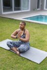 Konzentrierte afrikanisch-amerikanische Plus-Size-Frau praktiziert Yoga auf Matte im Garten. Fitness und gesunder, aktiver Lebensstil. — Stockfoto