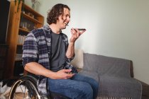 Caucásico hombre discapacitado sentado en silla de ruedas hablando en el teléfono inteligente en casa. concepto de discapacidad y discapacidad - foto de stock