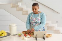 Africano americano más tamaño mujer cortando verduras, utilizando tableta en la cocina. estilo de vida, cocinar y pasar tiempo en casa. - foto de stock