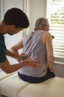 Fisioterapeuta masculino biracial tratando costas de paciente masculino sênior na clínica. cuidados de saúde seniores e tratamento de fisioterapia médica. — Fotografia de Stock