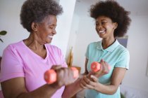Sorrindo afro-americana fisioterapeuta do sexo feminino tratando braços de paciente sênior na clínica. cuidados de saúde seniores e tratamento de fisioterapia médica. — Fotografia de Stock