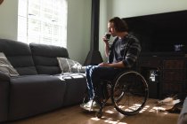 Pensativo hombre caucásico discapacitado sentado en silla de ruedas bebiendo café en casa. concepto de discapacidad y discapacidad - foto de stock