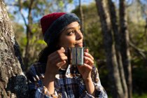 Happy biracial woman drinking coffee and taking break from hiking in countryside. healthy, active outdoor lifestyle and leisure time. — Stock Photo