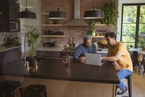 Biracial erwachsener Sohn und älterer Vater mit Laptop in der Küche. Familienzeit zu Hause zusammen. — Stockfoto