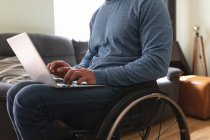 Средняя часть инвалида сидит на инвалидной коляске с ноутбуком дома. Концепция инвалидности и инвалидности — стоковое фото