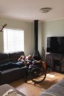 Kaukasischer Behinderter trägt Kopfhörer mit Smartphone, während er zu Hause auf der Couch liegt. Behinderten- und Behindertenkonzept — Stockfoto