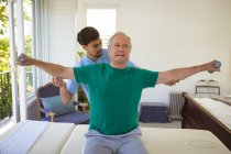 Fisioterapeuta masculino biracial tratando costas de paciente masculino sênior na clínica. cuidados de saúde seniores e tratamento de fisioterapia médica. — Fotografia de Stock