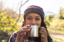 Mujer birracial feliz bebiendo café y tomando un descanso de senderismo en el campo. estilo de vida al aire libre saludable y activo y tiempo libre. - foto de stock