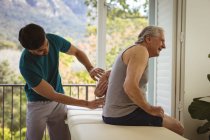Physiothérapeute mâle naissante soignant le dos d'un patient masculin âgé à la clinique. soins de santé supérieurs et traitement de physiothérapie médicale. — Photo de stock