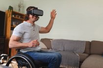 Caucasian disabled man sitting on wheelchair wearing vr headset and gesturing at home. disability and handicap concept — Stock Photo