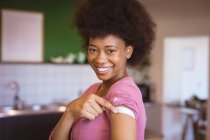 Портрет усміхненої афро-американської жінки, що зображає пов'язку на руці після вакцинації. Охорона здоров 