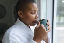 Femme afro-américaine détendue plus la taille buvant du café à la maison. mode de vie, loisirs et passer du temps à la maison. — Photo de stock