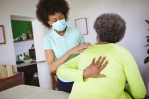 Африканська американська жінка-фізіотерапевт, яка лікує старшого пацієнта з масками обличчя в клініці. Вища медична допомога та фізіотерапія. — стокове фото
