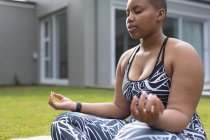 Focada afro-americana plus size mulher praticando ioga no tapete no jardim. fitness e estilo de vida saudável e ativo. — Fotografia de Stock
