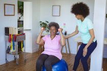 Fisioterapista afro-americana sorridente che cura la schiena di una paziente anziana della clinica. assistenza sanitaria senior e trattamento fisioterapico medico. — Foto stock