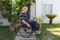 Retrato de hombre caucásico discapacitado sentado en silla de ruedas sonriendo en el jardín. concepto de discapacidad y discapacidad - foto de stock