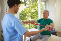 Zweirassiger männlicher Physiotherapeut, der Arme eines älteren männlichen Patienten in der Klinik behandelt. Senior Health und medizinische physiotherapeutische Behandlung. — Stockfoto