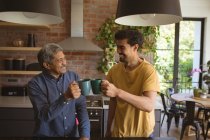 Sorrindo biracial filho adulto e pai sênior beber café na cozinha. tempo de família em casa juntos. — Fotografia de Stock