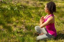 Relaxing biracial woman practicing yoga, sitting with crossed legs and meditating in countryside. healthy, active outdoor lifestyle and leisure time. — Stock Photo