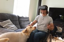Kaukasischer behinderter Mann mit Kopfhörer, der im Rollstuhl sitzt und zu Hause seinen Hund berührt. Behinderten- und Behindertenkonzept — Stockfoto