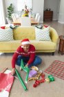 Heureux afro-américain plus femme taille dans santa chapeau enveloppant cadeaux à la maison. Noël, fête et concept de tradition. — Photo de stock