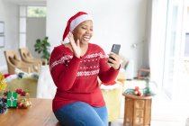 Feliz afro-americano plus size mulher em santa chapéu fazendo chamada de vídeo de Natal no smartphone. Natal, festividade e tecnologia de comunicação. — Fotografia de Stock