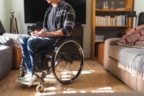 Mittlerer Abschnitt des kaukasischen behinderten Mannes, der im Rollstuhl sitzt und zu Hause sein Smartphone benutzt. Behinderten- und Behindertenkonzept — Stockfoto