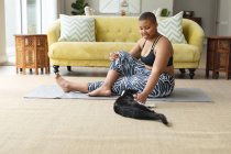 Счастливый африканский американец плюс размер женщина практикует йогу на коврике дома с котом. фитнес и здоровый, активный образ жизни. — стоковое фото