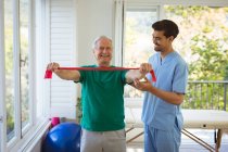 Smiling biracial male physiotherapist treating back of senior male patient at clinic. senior healthcare and medical physiotherapy treatment. — Stock Photo