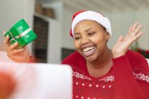 Счастливый африканский американец плюс женщина в шляпе Санты делает рождественский видеозвонок на ноутбуке. Рождество, праздник и коммуникационные технологии. — стоковое фото