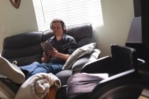 Homem deficiente caucasiano usando fones de ouvido usando tablet digital sentado no sofá em casa. conceito de deficiência e deficiência — Fotografia de Stock